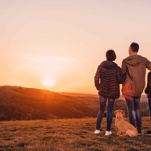 Family with dog embracing at hill and looking at sunset