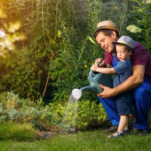 little boy and happy grandfather gardener with watering can in garden
