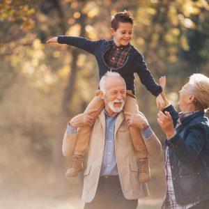 Smiling grandson walking through autumn park with grandparents.